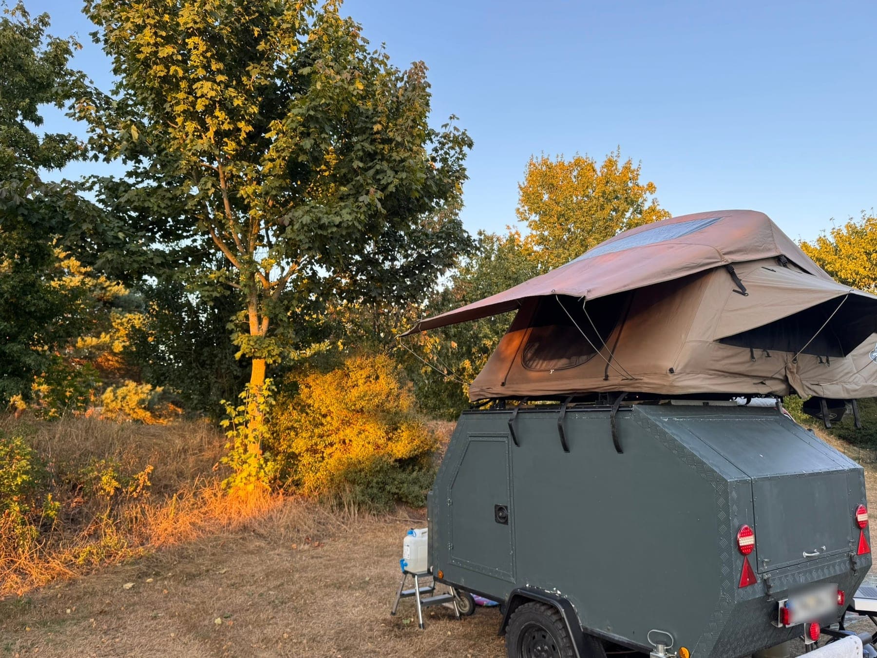 Offroad-Anhänger mit aufgebautem Dachzelt auf einer Wiese im Abendlicht